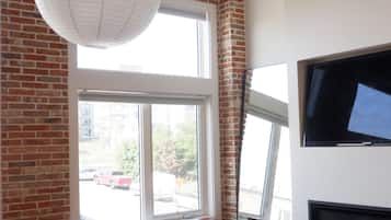 A modern room with a brick wall, a large window, a red bench, a flat-screen TV mounted on the wall, and a hanging light fixture.