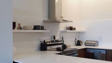 A modern kitchen with white countertops, a built-in oven, a stove, and a dishwasher. There are three black bar stools and a wooden bar counter.