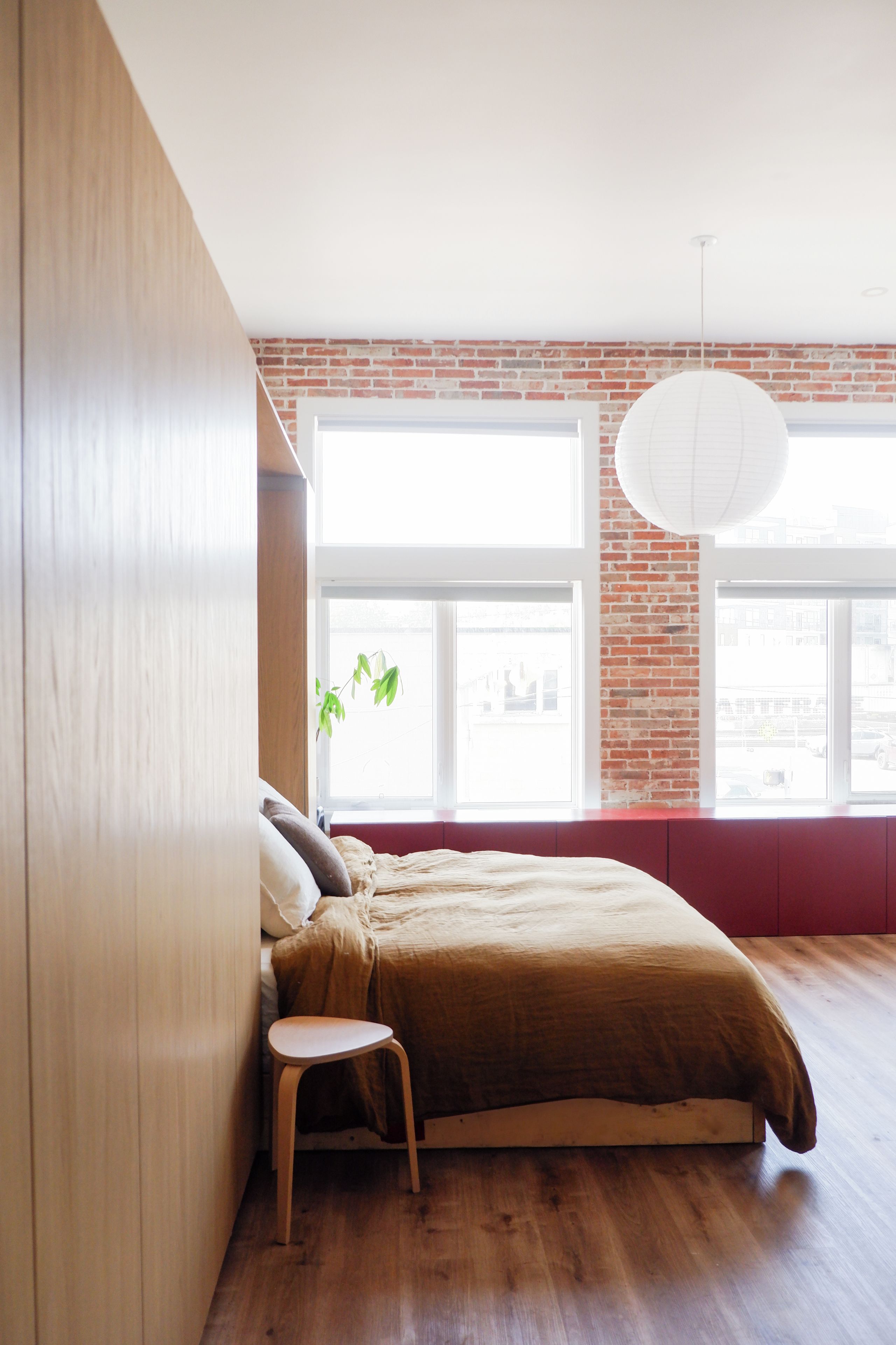 A bedroom with a large window, a bed, a chair, and a hanging light fixture.