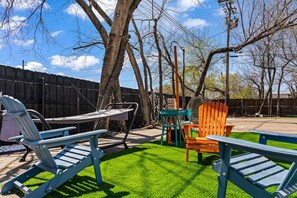 A backyard with a lawn, a wooden fence, and outdoor furniture including a table and chairs. - Stylish & Comfy Downtown Gem ~ Workspace ~ Parking (Irving)