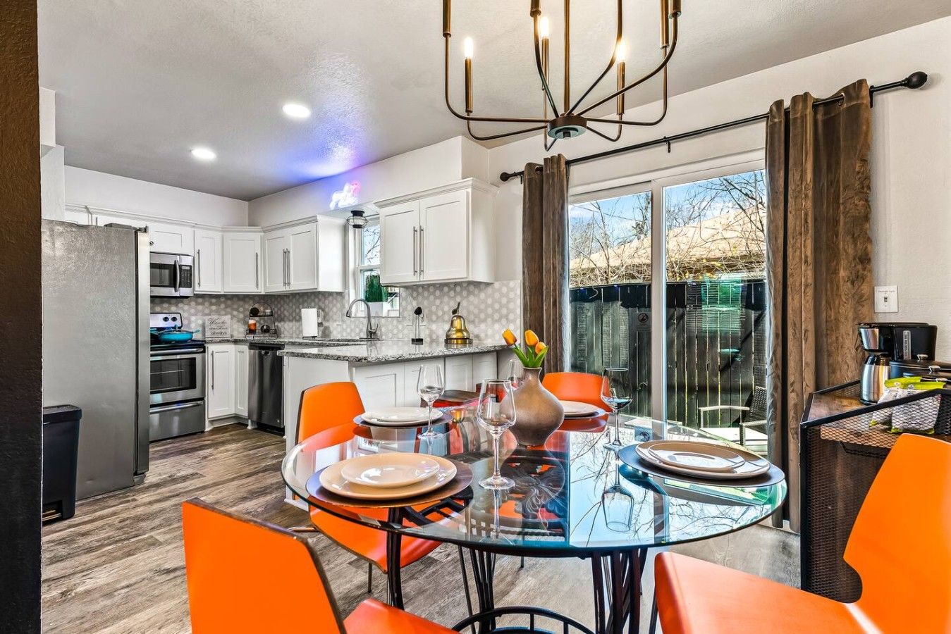 Une cuisine moderne avec des armoires blanches, une cuisinière en acier inoxydable et un coin repas doté de chaises orange et d’une table en verre.