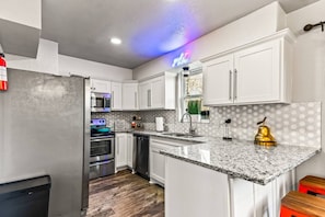 A modern kitchen with white cabinets, a granite countertop, stainless steel appliances, and a neon sign. - Stylish & Comfy Downtown Gem ~ Workspace ~ Parking (Irving)