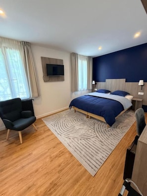A modern hotel room with a bed, a TV, a chair, and a view of the outdoors. - Laulique (Les Lilas)