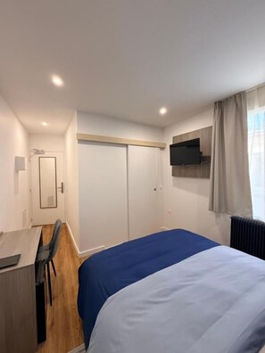 A hotel room with a bed, a desk, a chair, a television, and a window with curtains.