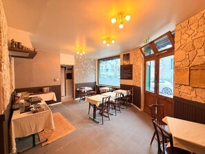 A restaurant interior with tables, chairs, a stone wall, and a view through the window.