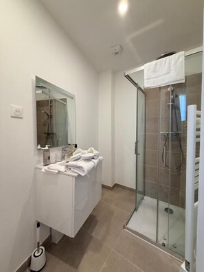 A modern bathroom with a glass shower enclosure, a white vanity, and a mirror. - Laulique (Les Lilas)