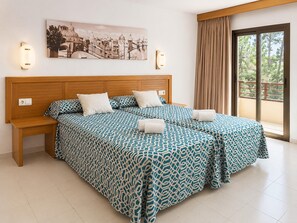 Ein Doppelbett mit gemusterten Betttextilien, ein Holz-Kopfteil, Nachttische, Wandleuchten, ein Stadtbildgemälde und ein Balkon mit Vorhängen.