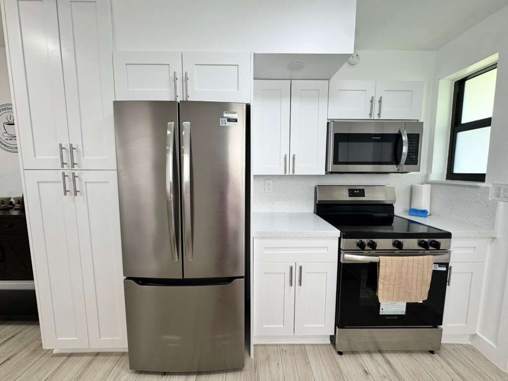 A modern kitchen with white cabinetry, a stainless steel refrigerator, a microwave, and a stove.