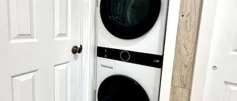 Una sala de lavandería con dos lavadoras apiladas, una puerta blanca y piso de madera.