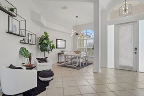 A modern living room with a white sofa, a dining table with chairs, a large plant, and a black rug. - Waterfront Oasis • Pool •  Private Dock • Firepit (Marco Island)