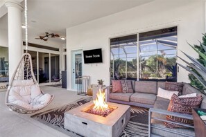 A modern living room with a fire pit, comfortable seating, and a large window overlooking a garden. - Waterfront Oasis • Pool •  Private Dock • Firepit (Marco Island)
