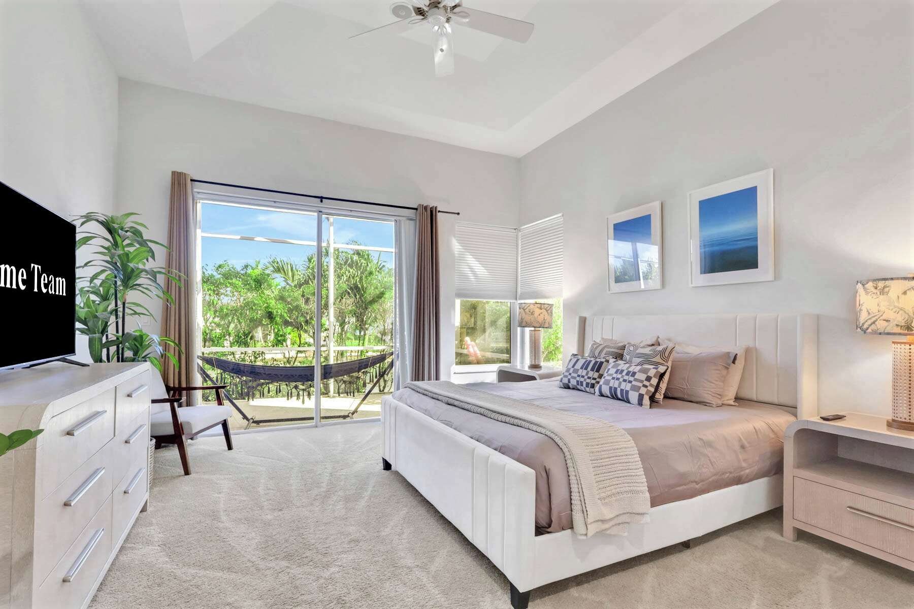 A modern bedroom with a large bed, a TV, a desk, and a balcony with a view of greenery.