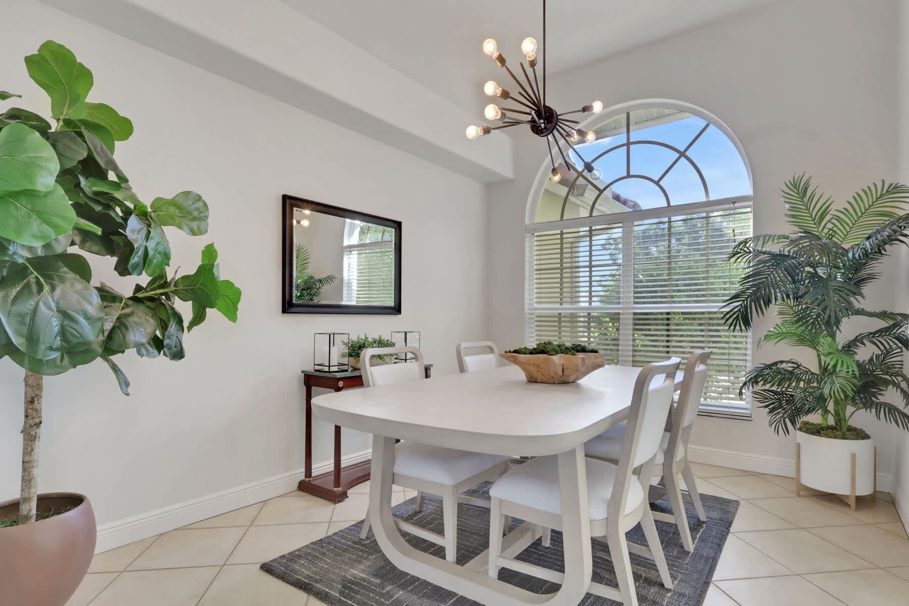 A dining area with a white table, chairs, a chandelier, and potted plants.