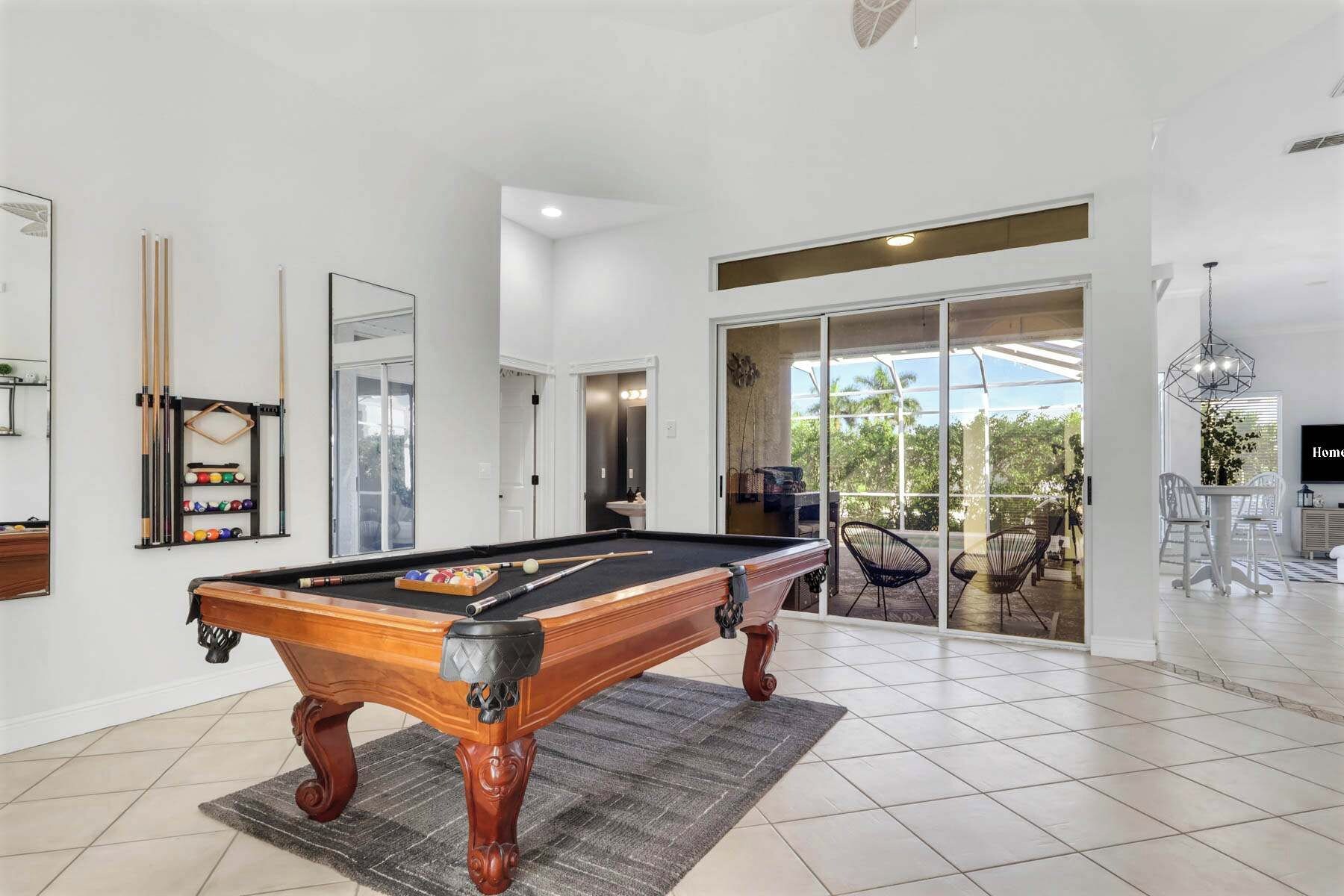 A pool table in a room with a large sliding glass door leading to an outdoor area with chairs.