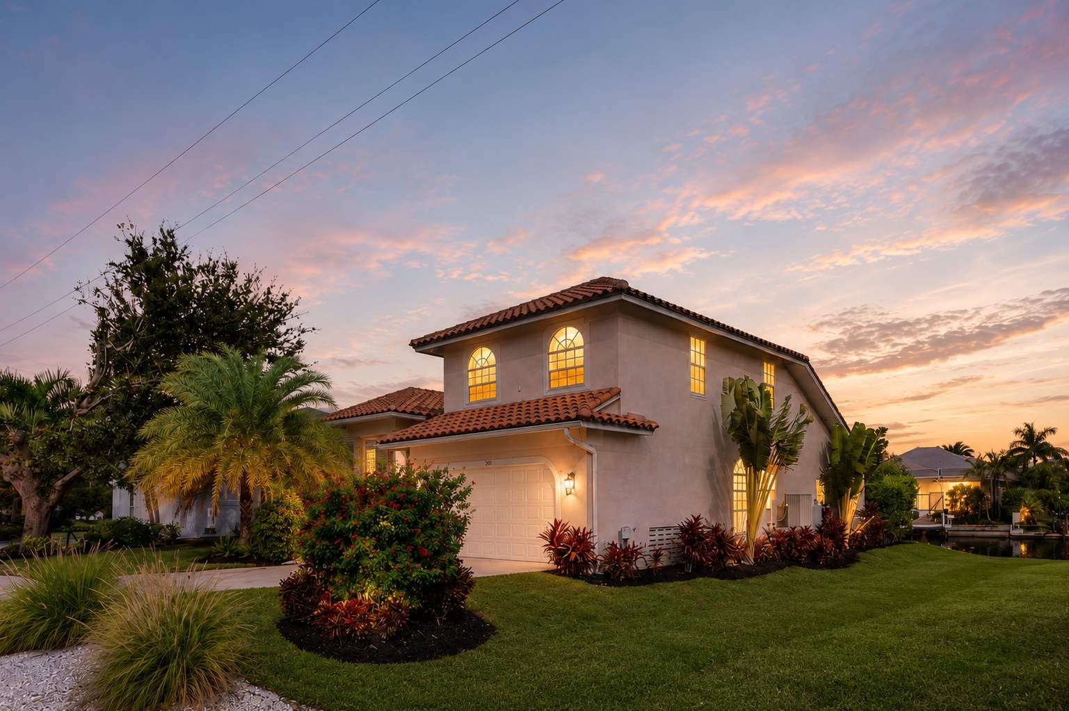 A two-story house with a tiled roof, a garage, and a well-maintained lawn with various plants.