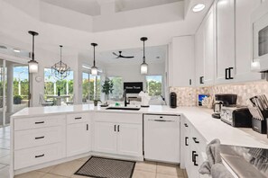 A modern kitchen with white cabinetry, a central island, overhead pendant lights, and a view of the outdoors. - Waterfront Oasis • Pool •  Private Dock • Firepit (Marco Island)