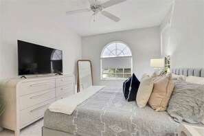 A bedroom with a bed, a dresser, a television, a ceiling fan, and a window with a view. - Waterfront Oasis • Pool •  Private Dock • Firepit (Marco Island)