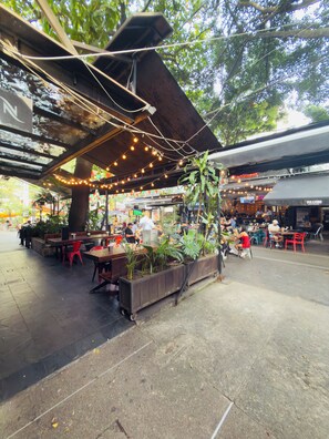 An outdoor seating area with tables and chairs, surrounded by greenery and string lights. - Charming 2-bedroom apartment with AC in vibrant Provenza (Medellín)