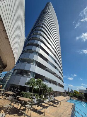 Un hôtel moderne à la façade incurvée, doté d’une piscine extérieure et d’un espace détente avec des fauteuils et des tables.