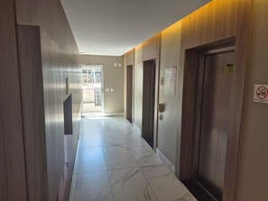 Un couloir doté d’un sol en marbre, de lambris en bois sur les murs et d’une porte sur laquelle est apposé un panneau « interdiction de fumer ».
