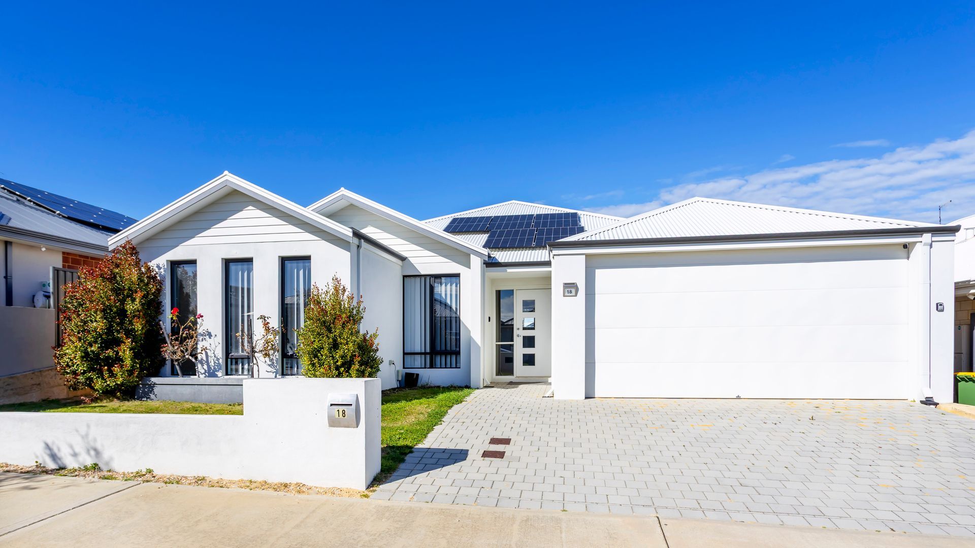A modern two-story house with a garage, solar panels, and a well-maintained front yard.