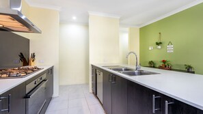A modern kitchen with a gas stove, stainless steel sink, and dark cabinetry. - Lakelands Escape Western Australia (Lakelands)