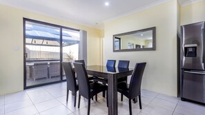 A dining area with a table and chairs, a refrigerator, and a sliding glass door leading to an outdoor patio with solar panels. - Lakelands Escape Western Australia (Lakelands)