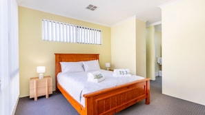 A hotel room with a wooden bed, two bedside tables, a window with blinds, and a bathroom visible through an open door. - Lakelands Escape Western Australia (Lakelands)