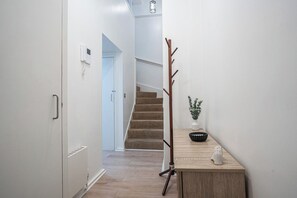 A hallway with a staircase, a coat rack, a small table with a plant, and a wall-mounted phone. - 2BR Flat - Greenwich - Parking - Elizabeth Line (Greater London)