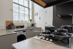 Moderni keittiö, jossa on sisäänrakennettu pesukone, liesi ja erilaisia ruoanlaittovälineitä.
