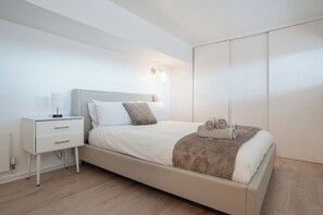 A modern bedroom with a bed, bedside table, and wardrobe. - 2BR Flat - Greenwich - Parking - Elizabeth Line (Greater London)