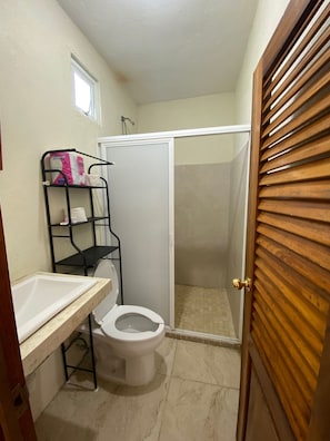 Ein kleines Badezimmer mit Toilette, Waschbecken, Dusche und einem Ablagefach für Pflegeprodukte.