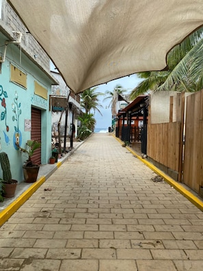 Rua pavimentada com edifícios em ambos os lados, alguns com letreiros visíveis, e uma cerca de madeira à direita.