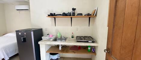 A compact kitchenette with a refrigerator, sink, and gas stove.