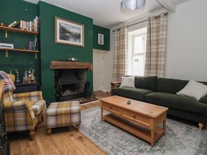 A cozy living room with a fireplace, green walls, a sofa, a coffee table, and a plaid armchair. - Bowdery (Harrogate)