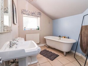 A bathroom with a white sink, a freestanding bathtub, a window with blinds, and a radiator. - Bowdery (Harrogate)