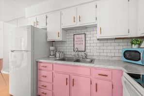 A kitchen with white cabinets, a pink countertop, and a blue microwave. - Glam Society Music Row-IG Worthy-Outdoor Lounge (Nashville)