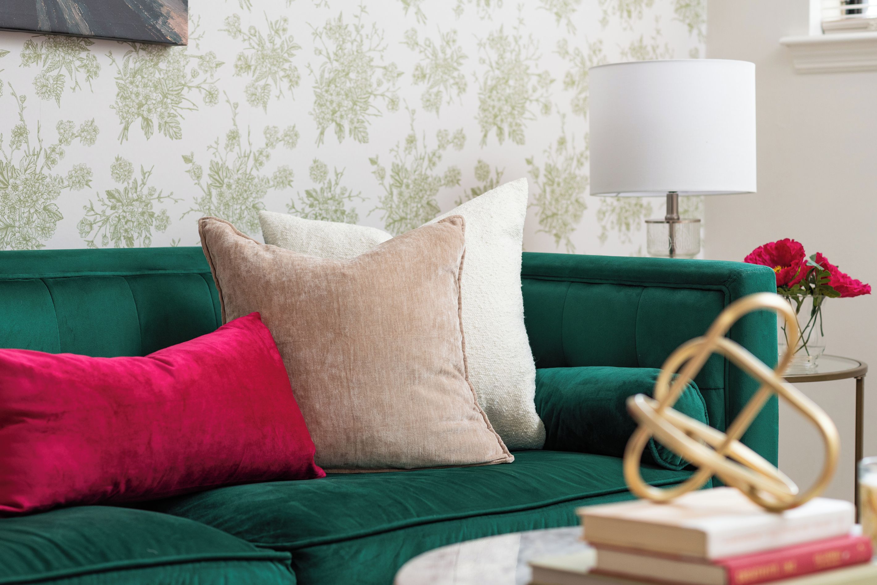 Ein grünes Sofa mit vielen Kissen, einer weißen Lampe und einer Blumenvase.