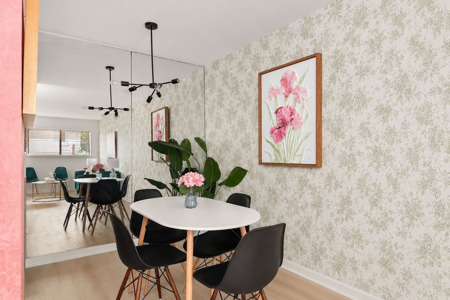 Un comedor con una mesa redonda, sillas negras y un florero con flores rosadas.