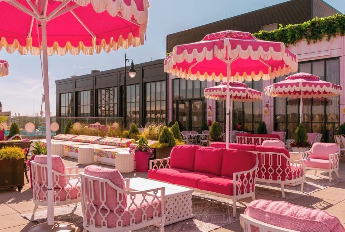 An outdoor seating area with white and pink furniture, including sofas and chairs, under large pink umbrellas.