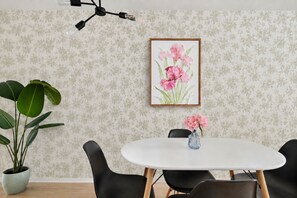 Un coin repas avec une table ronde, des chaises noires, une plante en pot, une œuvre d’art florale encadrée et un luminaire suspendu.