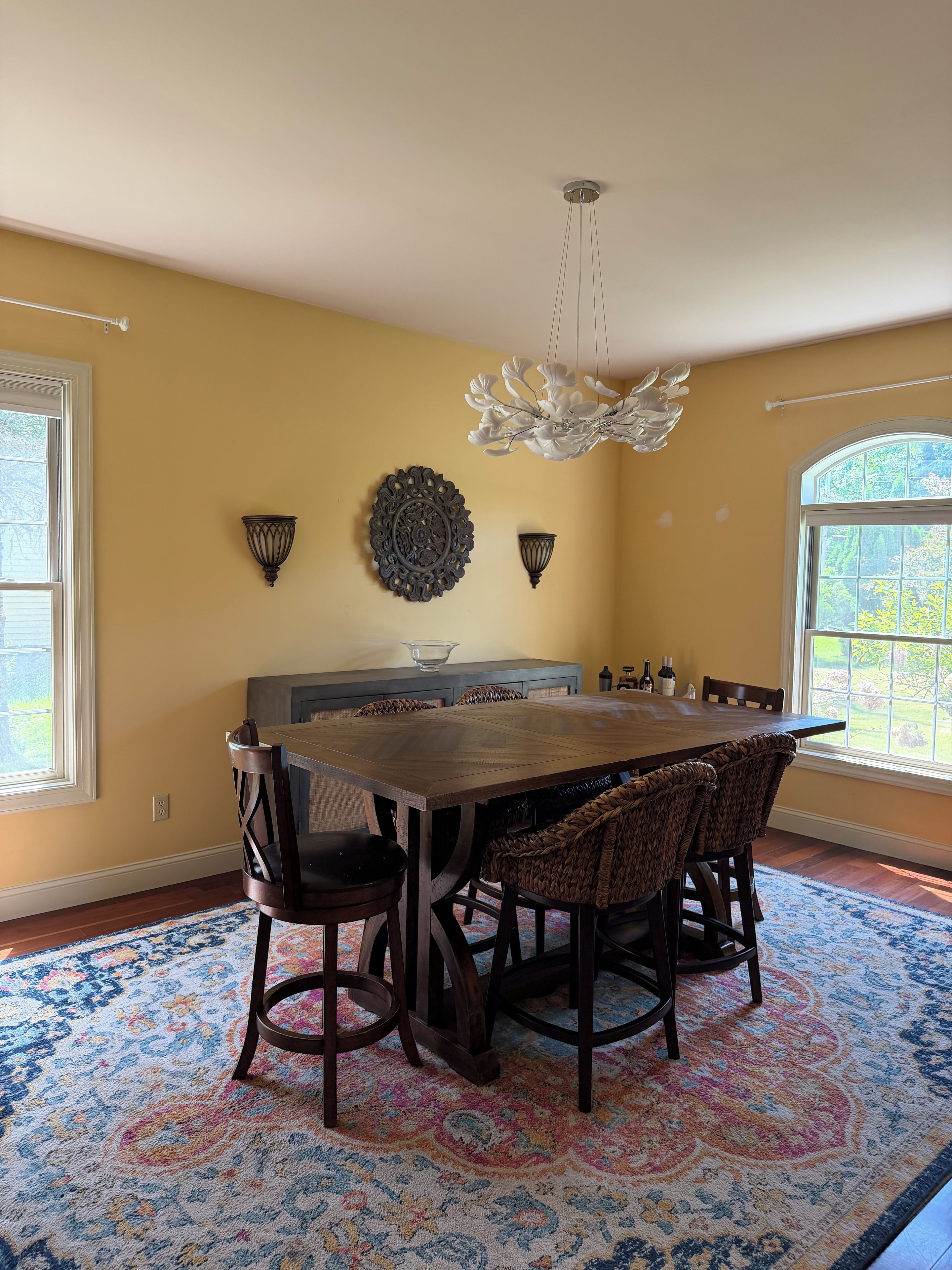 A dining room with a large wooden table, dark chairs, and a patterned rug.