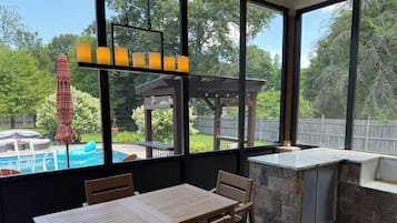 A patio area with a pool, wooden furniture, and a stone bar.
