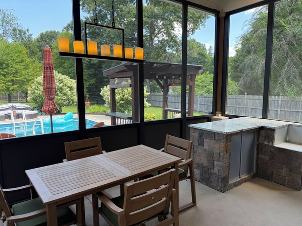 A patio area with a pool, wooden furniture, and a stone bar.