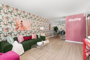 A living room with a floral wallpaper, a green sofa, a clear coffee table, and a pink accent wall. - House of Pearls Glam Stay on Music Row IG Worthy (Nashville)