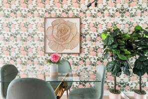 A room with a floral wallpaper, a framed artwork, a potted plant, and a glass table with chairs. - House of Pearls Glam Stay on Music Row IG Worthy (Nashville)