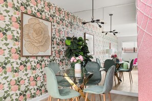 A dining area with a floral wallpaper, a glass table, and modern chairs. - House of Pearls Glam Stay on Music Row IG Worthy (Nashville)