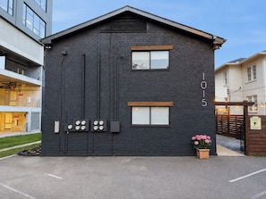 Een modern gebouw met een donkere gevel, huisnummer 1015, met een grote deur, meerdere ramen en een kleine bloempot op de grond.