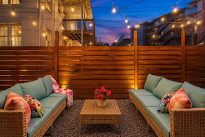 An outdoor seating area with wicker furniture and a central table, surrounded by a wooden fence and string lights. - Legends Lounge Glam Suite On Music Row IG Worthy (Nashville)