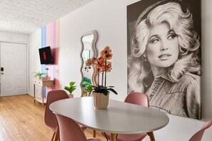 Ein modernes Wohnzimmer mit einem runden Tisch, rosafarbenen Stühlen, einem an der Wand montierten Flachbildfernseher und einem großen gerahmten Porträt.